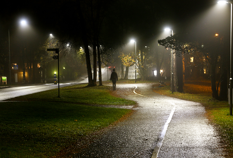 En person går på gångväg i dimma medan ljuslyktor lyser upp