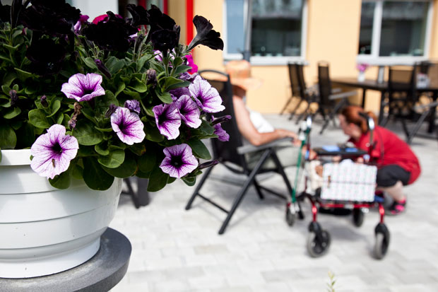 Äldre dam med vårdpersonal och blommor i förgrunden