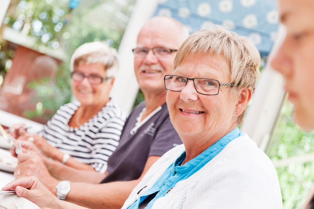 Leende äldre män och kvinnor som sitter vid ett matbord.