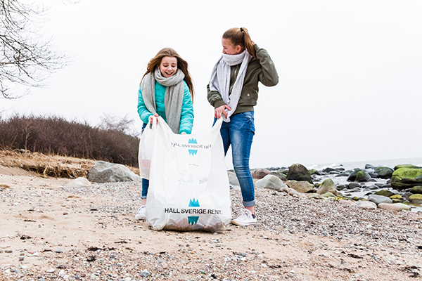 Två flickor som går fyller en stor säck med skräp på en blåsig strand.