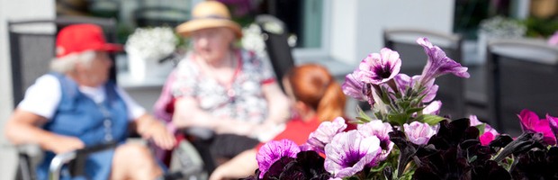 Två äldre damer sitter ute i solen med blomlådor i förgrunden