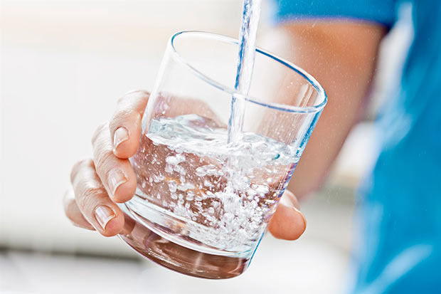 En hand som håller i ett glas som fylls med rent vatten från en kran