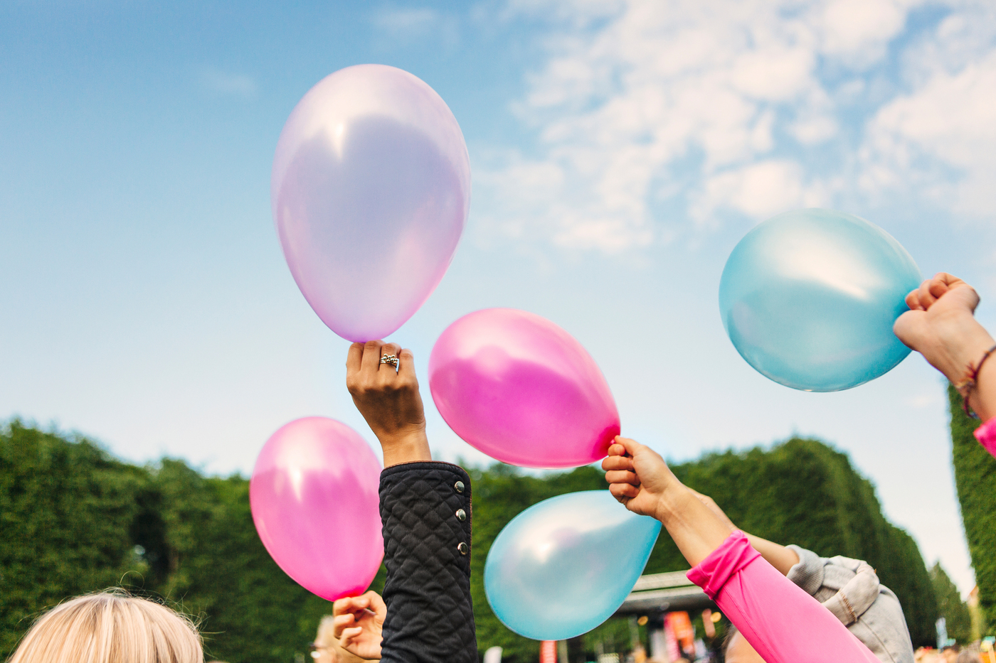 Ballonger i olika färger som hålls upp mot himlen av händer