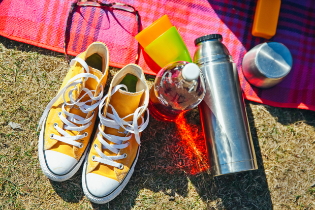 Närbilid på picknickfilt med termos, dricka och skor