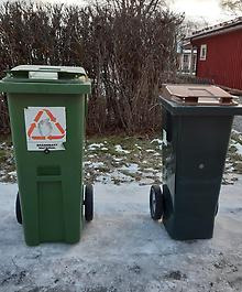 Två soptunnor står med draghandtagen vända bort från vägen. De står en bit in på vägen och med en halvmeters mellanrum.