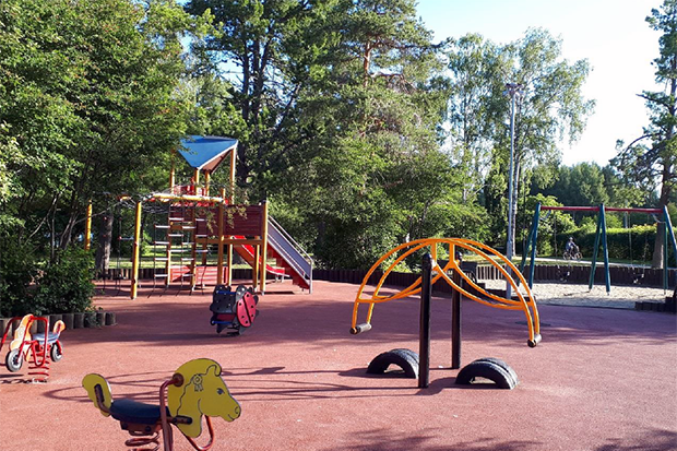 Lekplats med fjädergungor, gungor och ett lekhus i bakgrunden