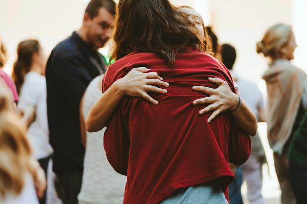 Två personer kramar varandra tätt i en folksamling, med fokus på deras armar och ryggar medan omgivningen är suddig i bakgrunden.