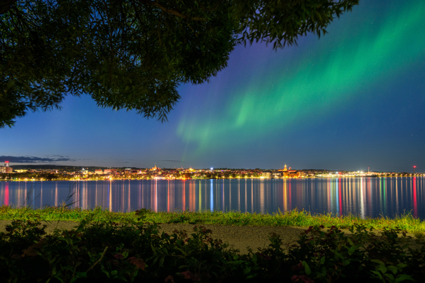 Nattvy över Östersund från Frösön. med norrsken och vackra speglingar i vattnet.