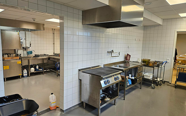 köksinteriör med spis, diskmaskin, diskbänk mot skinande vita kakelväggar.