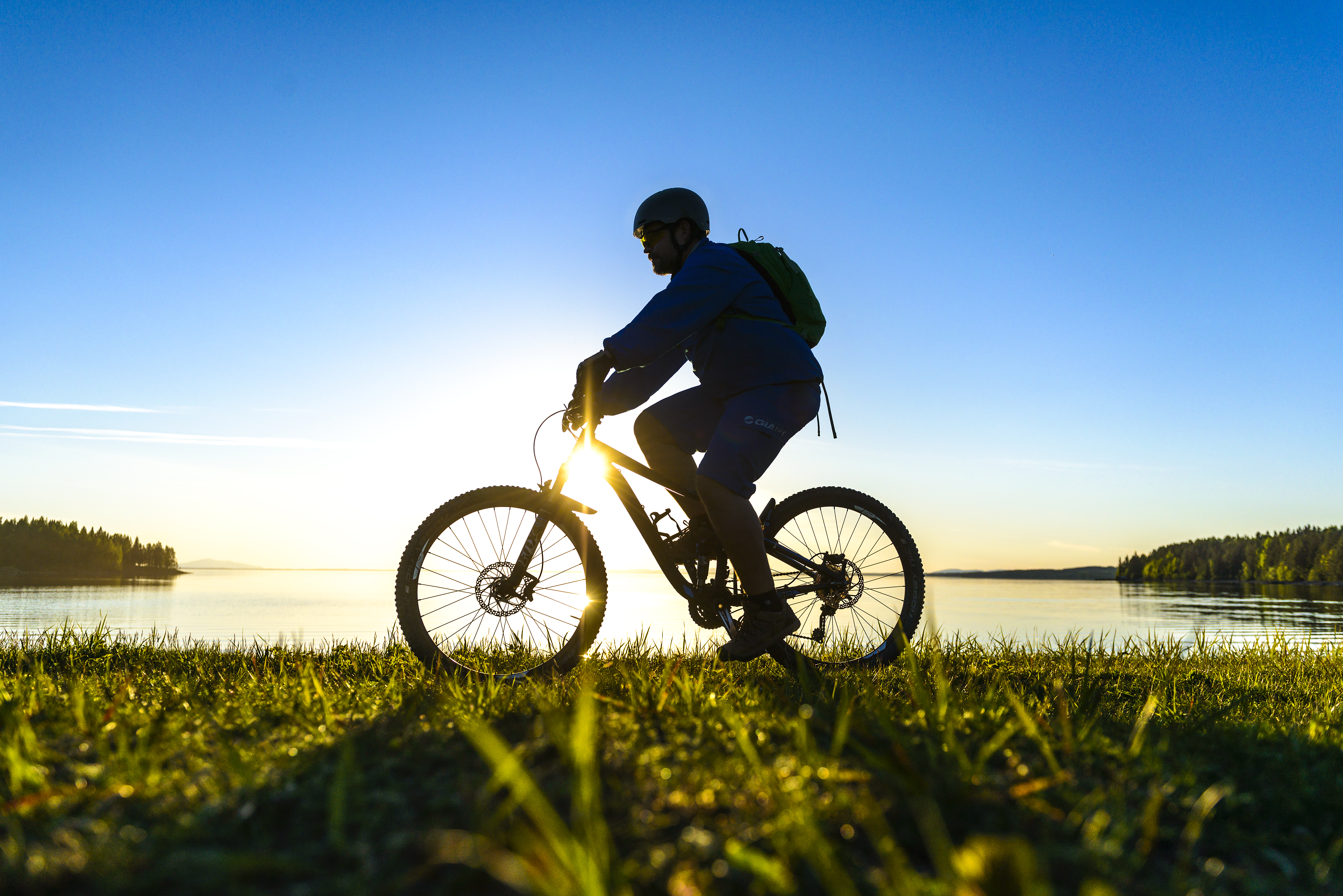 Bild på en cyklist vid en sjö under en solnedgång.