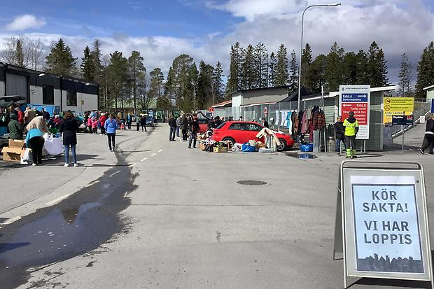 Skylt  förgrunden. I bakgrunden människor och bilar med bakluckorna öppnade