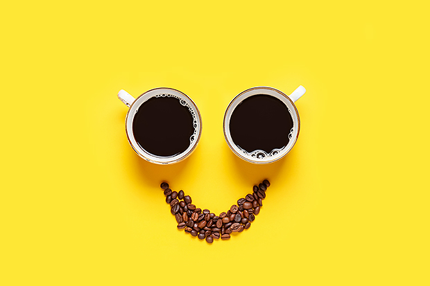 Två kaffekoppar bildar ögon i en figur där en näve kaffebönor formats till en leende mun.