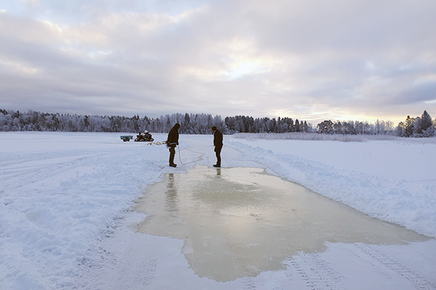 Vacker vinterhimmel över sjöis och en plogad bana där två män spolar isen
