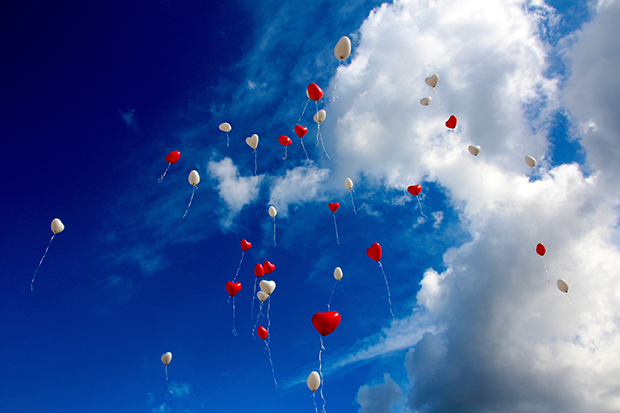 Blå himmel med vita moln och hjärtformade ballonger som stiger mot himlen