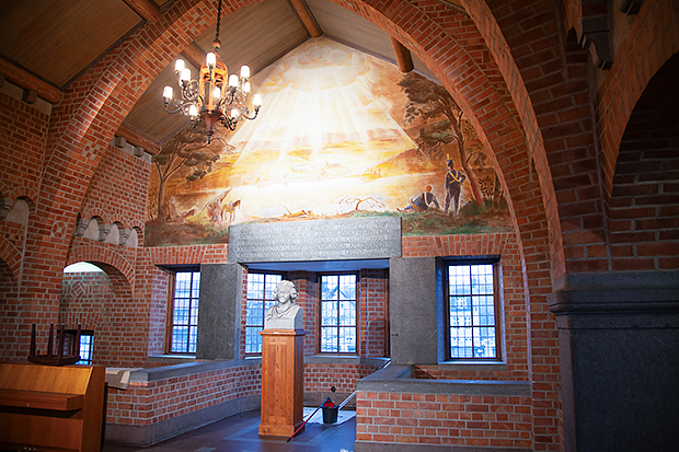 Inredningen i ett kyrkliknande rum med röd tegelarkitektur, spetsbågiga valv och blyinfattade fönster. En marmorbyst står på sockel mitt i rummet. Ovanför syns en stor väggmålning med ljusstrålar som faller ner från himlen, omgiven av ett pastoralt landskap med människor och träd. En ljuskrona hänger i taket och kastar varmt ljus över rummet.