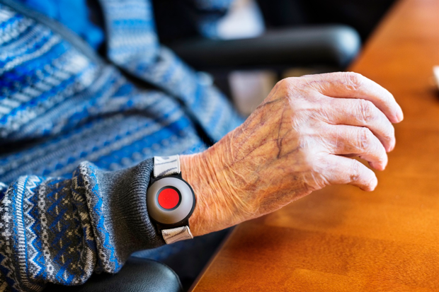 Ett trygghetslarm på ett armband kring en handled på en äldre människa.