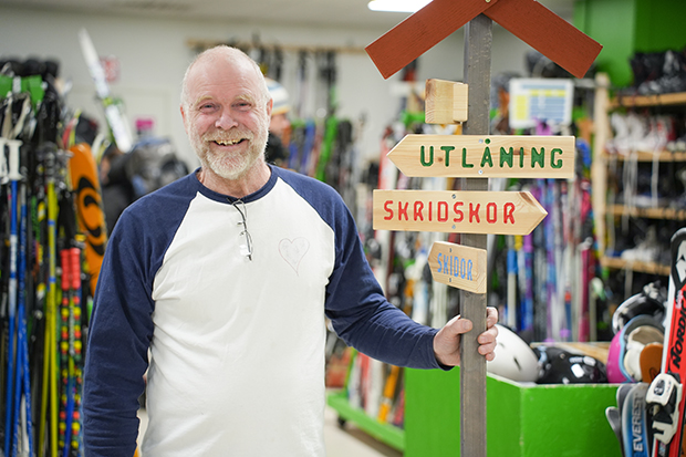 En glad man står mitt i bild intill en skylt där det står utlåning och skridskor