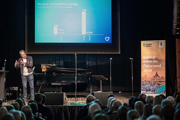 En man står på en scen tillsammans med en flygel, några mikrofoner och en roll-up.