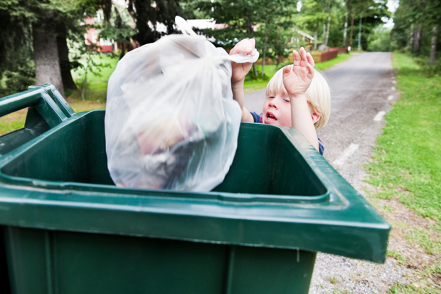 Ett barn kastar en soppåse i en grön soptunna.