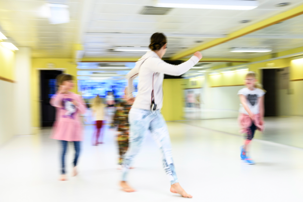 Barn och en vuxen i träningskläder som rör sig i en sporthall.