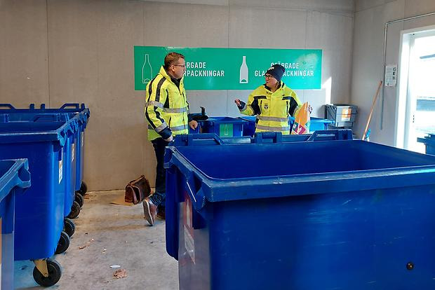 Två personer i iklädda varselkläder pratar i ett soprum