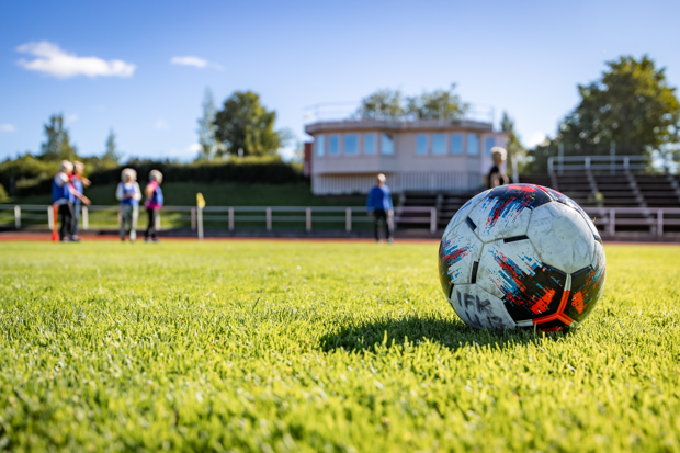 Fotboll på grnt gräs med människor i bakgrunden.