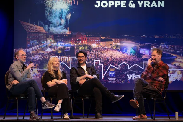tre män och en kvinna sitter på en scen och pratar