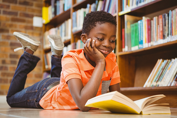 En pojke ligger på golvet i ett bibliotek och läser en bok