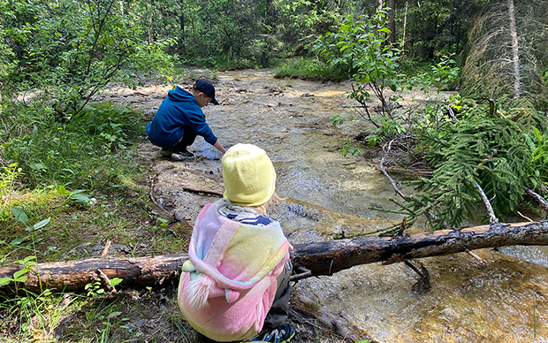 Två barn leker vid en bäck i skogen.