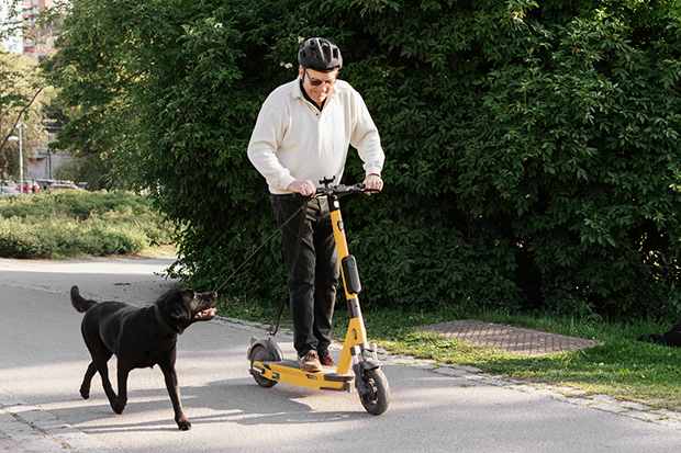Man med hjälm som åker elsparkcykel. Bredvid springer en hund