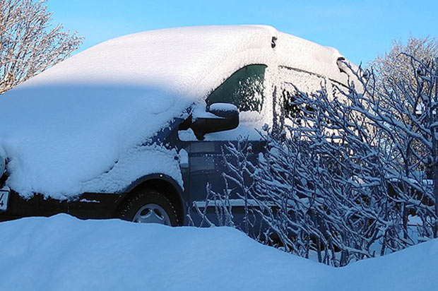 En översnöad bil som står bakom en snöplogkant