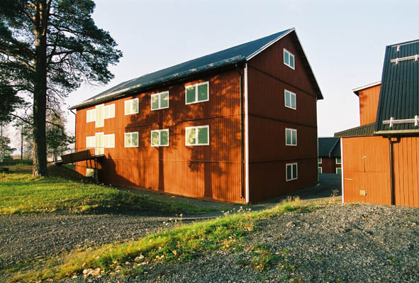 Lugnet 7, hus 36 - Gammal, röd förrådsbyggnad i tre våningar med gröna dörrar och gröna fönsterluckor.