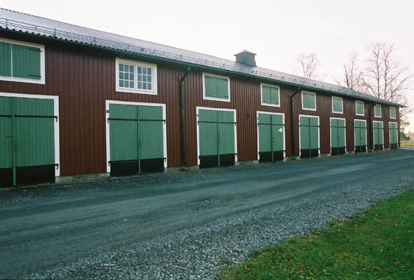 Lugnet 7, hus 43. Röd, gammal förrådsbyggnad i två våningar med gröna dörrar och fönsterluckor.