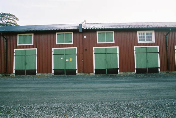 Lugnet 7, hus 43. Röd, gammal förrådsbyggnad i två våningar med gröna dörrar och fönsterluckor.