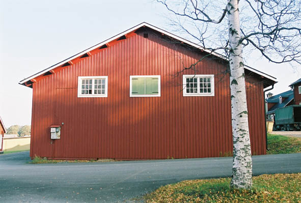 Lugnet 7, hus 43. Röd, gammal förrådsbyggnad i två våningar. Grön dörr och vitt fönster med spröjs.