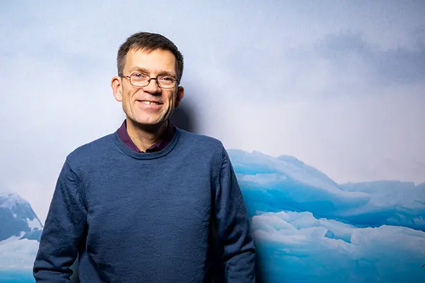 En glad man i blå tröja framför en blå vägg
