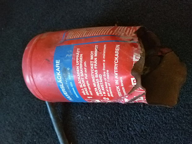 En röd brandsläckare som är söndersprängd. Bara övre halvan är kvar.