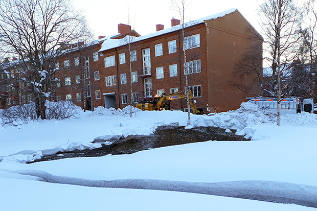 Vatten som bildat bäck i djup snö framför ett lägenhetshus.
