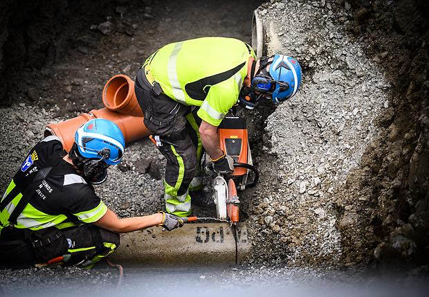 Två personer står böjda över ett arbete med ledningsrör.