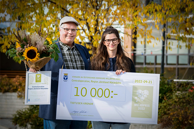 En man och kvinna står med stor prischeck framför gulnade löv