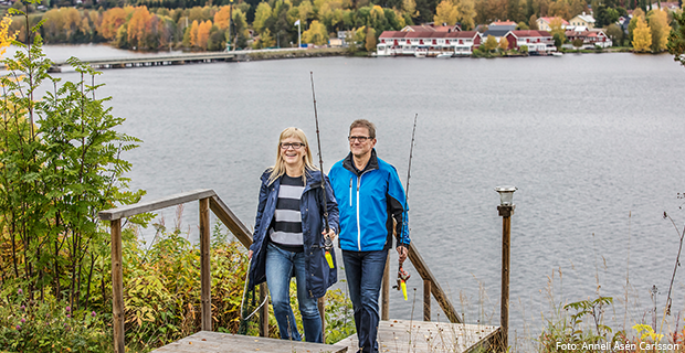 Två personer med fiskespö går uppför trappa från Indalsälven. Bro och bebyggelse i bakgrunden