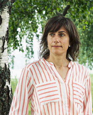 En kvinna i randig blus står vid en grönskande björk
