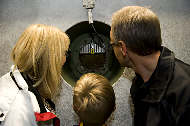 En kvinna, en man och ett barn tittar in i ett titthål in i vattenverket.