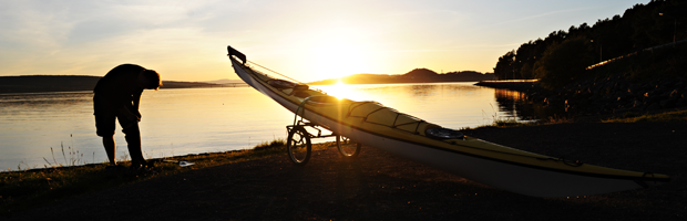 En person med en kanot som är uppdragen på land i solnedgång vid vatten