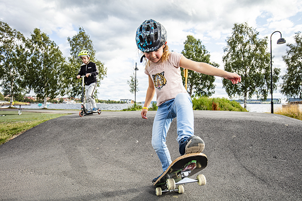 Ung flicka med hjälm som åker skateboard på en asfalterad bana.