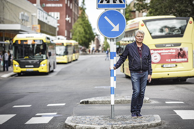En man står mitt på en central väg med busstrafik i bakgrunden.
