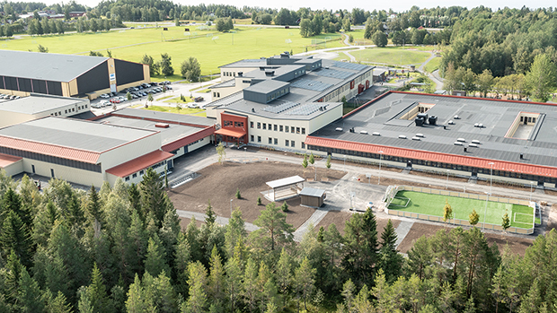Flygbild över Odensalaskolan. Man ser fotbollsplan, lekplats, asfaltsytor och parkeringar. Runt omkring syns skog och gröna fält.