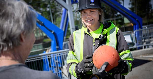 Person lämnar en röd boll till varselklädd person på återvinningscentralen