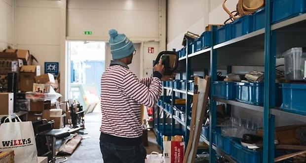 Person med randig tröja och mössa med tofs tar något från en hylla med blå plastbackar.