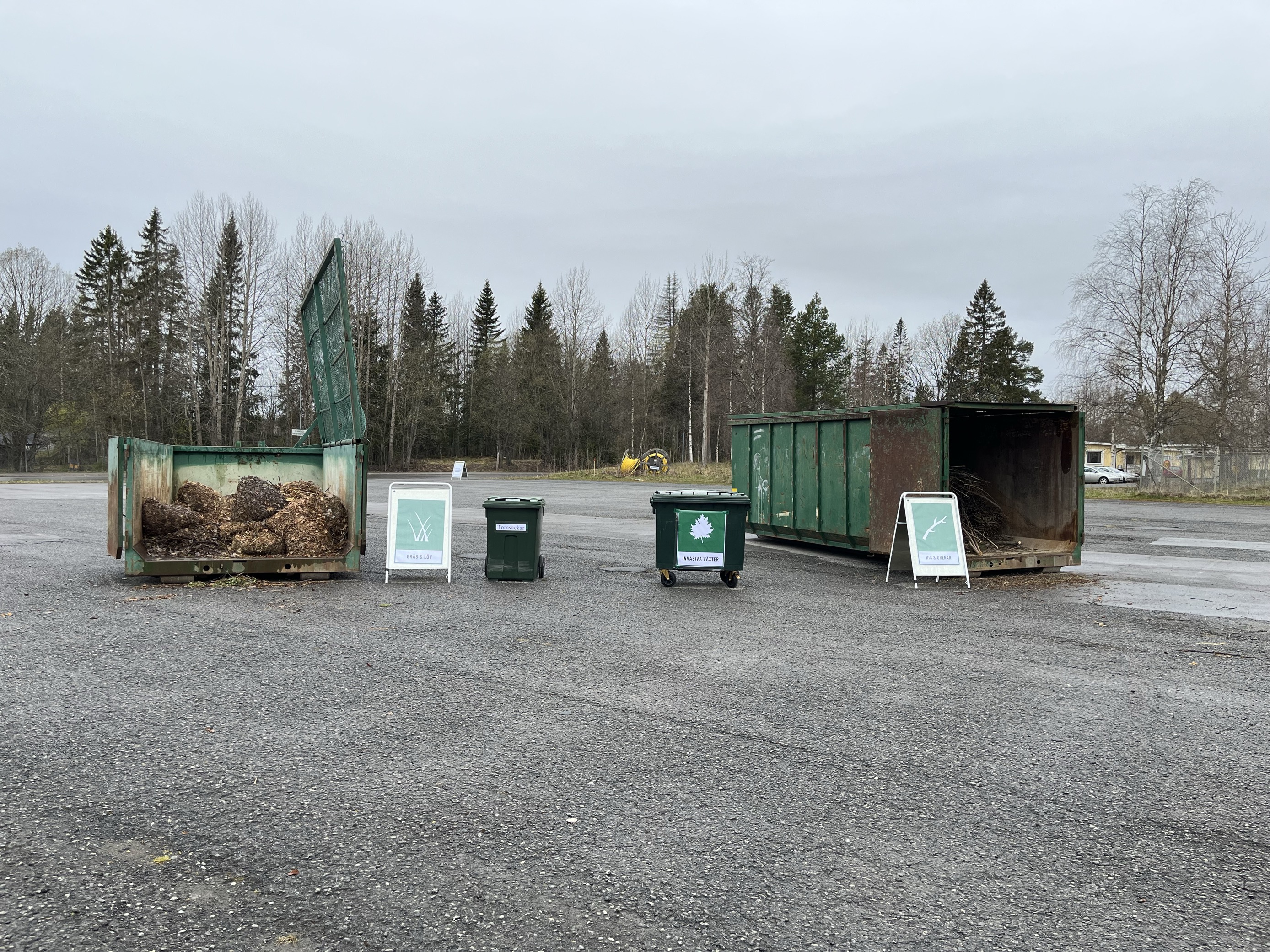 Tre behållare för trädgårdsavfall på en grusplan.